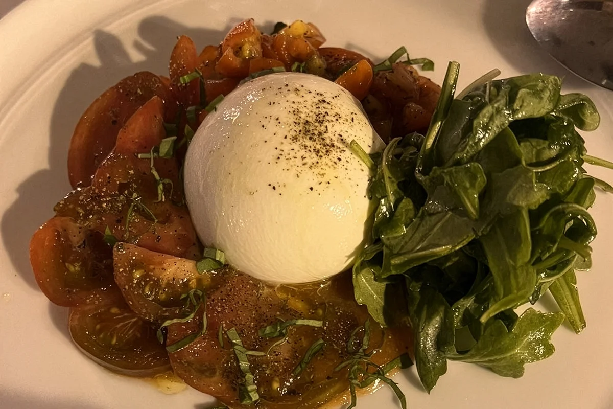 A fresh burrata cheese ball centered on a bed of sliced heirloom tomatoes and garnished with fresh basil and arugula.