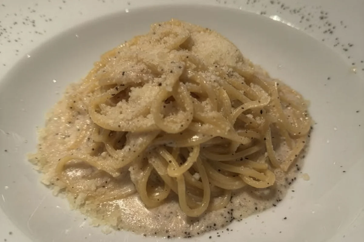 A close-up shot of creamy Cacio e Pepe pasta seasoned with cracked black pepper and grated Pecorino Romano cheese in a white bowl.