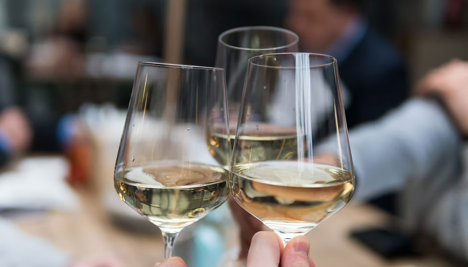 Three people toasting with glasses of white wine at an Italian restaurant.